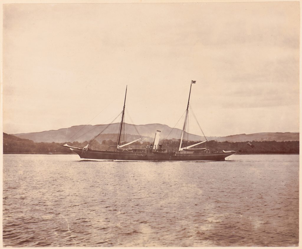 Brytyjski jacht parowy płynie ożaglowaniem gaflowym wzdłuż wybrzeża.