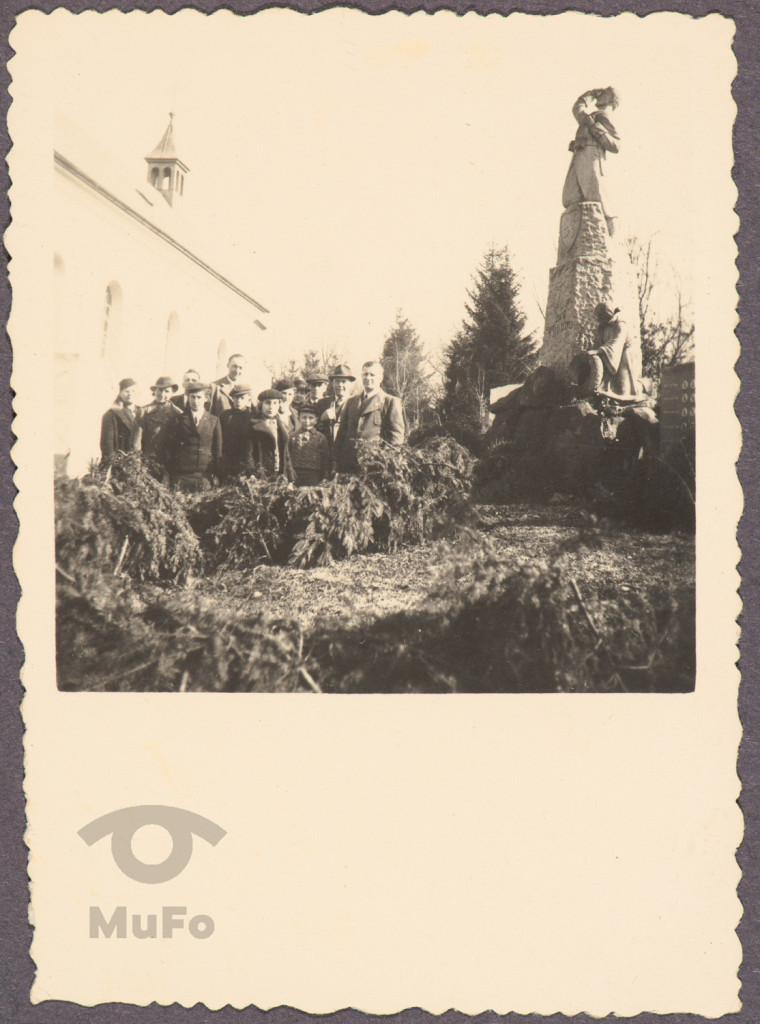 grupa trzynastu osób na tle pomnika i kościoła, portret