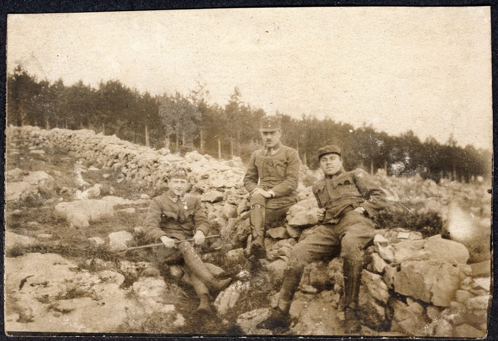 3. wojskowi  w mundurach armii austro-węgierskiej, portret zbiorowy w plenerze, siedzą na kamieniach pod kamiennym murkiem na tle lasu, fot. z albumu zw. temat. z frontem ros. w cz.I wojny świat.