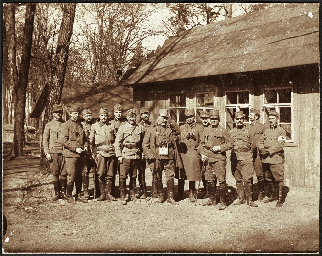 wojskowi  w mundurach armii austro-węgierskiej, 14. osób w szeregu; portret zbiorowy w plenerze, przed barakiem; fot. z albumu zw. temat. z frontem ros. w cz.I wojny świat.