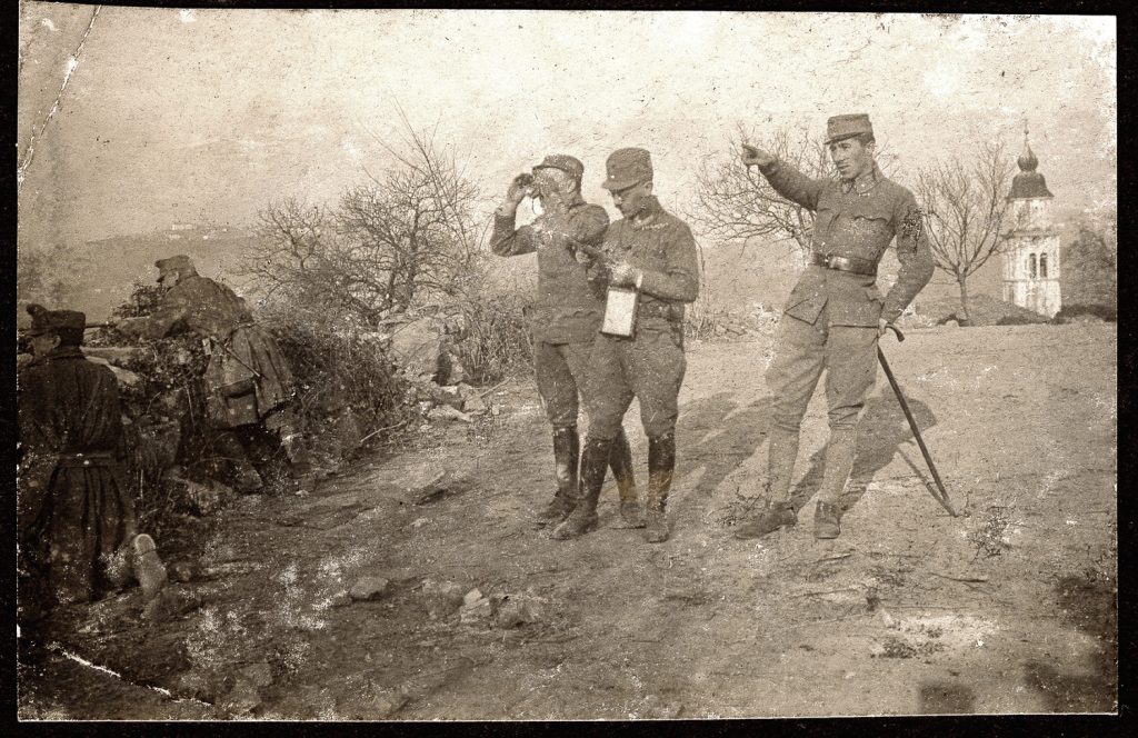3. wojskowi  w mundurach armii austro-węgierskiej, obserwator z lornetką i dwaj żołnierze na stanowiskach ogniowych; portret zbiorowy w plenerze, na tle wieży opatrzonej hełmem; fot. z albumu zw. temat. z frontem ros. w cz.I wojny świat.